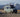 Custom Sprinter camper van with off-road tires parked on gravel with snowy mountain backdrop