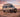 Custom Sprinter adventure van parked in desert at sunset, featuring off-road tires and palm decals.