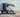 Custom Sprinter van with awning parked on sandy beach, person relaxing in chair nearby