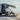 Custom Sprinter van with awning parked on sandy beach, person relaxing in chair nearby
