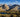 Scenic view of forested valley, alpine lake, and snow-capped mountains under blue sky