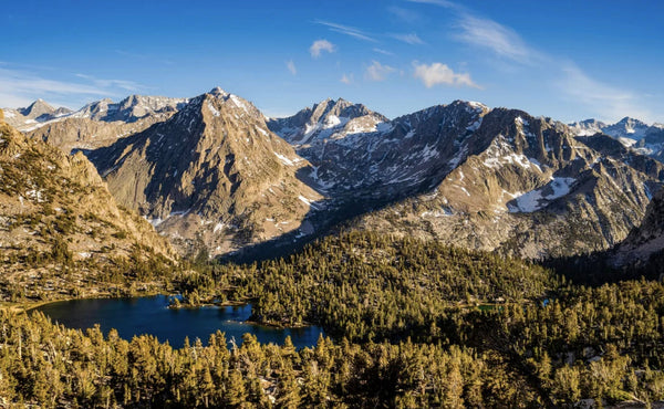 Scenic view of forested valley, alpine lake, and snow-capped mountains under blue sky