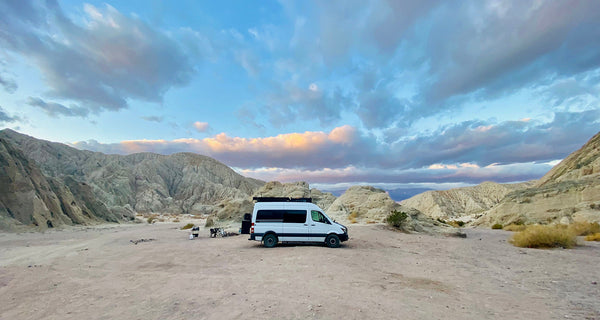 Custom camper van parked in a scenic desert canyon with rocky hills and blue sky