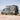 Custom Sprinter van with off-road tires and roof rack driving on a sandy beach