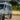 Custom Sprinter van with off-road tires, side ladder, roof rack, and LED lights in outdoor setting