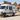 Custom Sprinter van with roof rack and exterior ladder parked in a rustic town setting