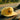 A yellow cap with a black Sandy Vans logo sits on the dashboard of a car, with a blurred road and green trees visible through the windshield in the background.