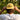 A man viewed from behind wearing a white t-shirt and a yellow cap with the Sandy Vans logo, adjusting the cap in an outdoor forest setting.