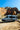 Blue Sprinter van with SV Side Ladder parked below red rock cliffs under a bright blue sky
