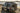 Custom Sprinter van with off-road tires and roof rack parked on sandy beach by the ocean
